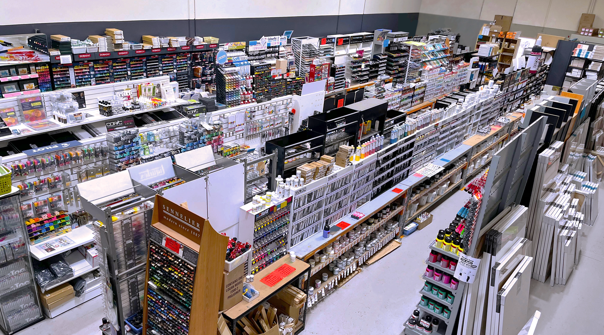 A birds eye view of The Art Shop floor, many stacked shelves in close aisles, all covered in art supplies like paint, brushes, mediums, markers, copics, pastels, canvas and more